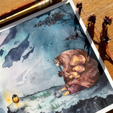 A square art print featuring a whimsical watercolor illustration of a large brown creature with yellow eyes and hands, sitting on a rocky shore under a blue sky. The print is styled on a wooden surface with paintbrushes and dried flowers.